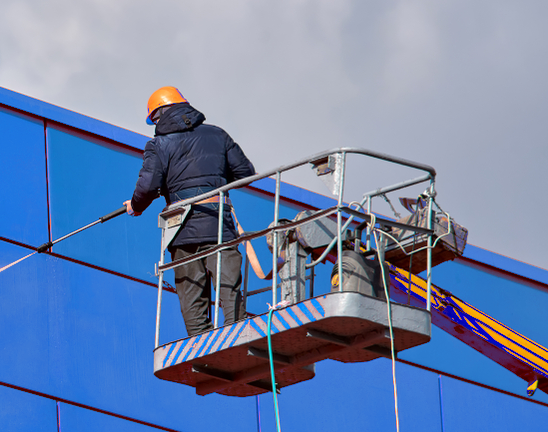 A power washing technician cleaning commercial siding with a cherry picker.