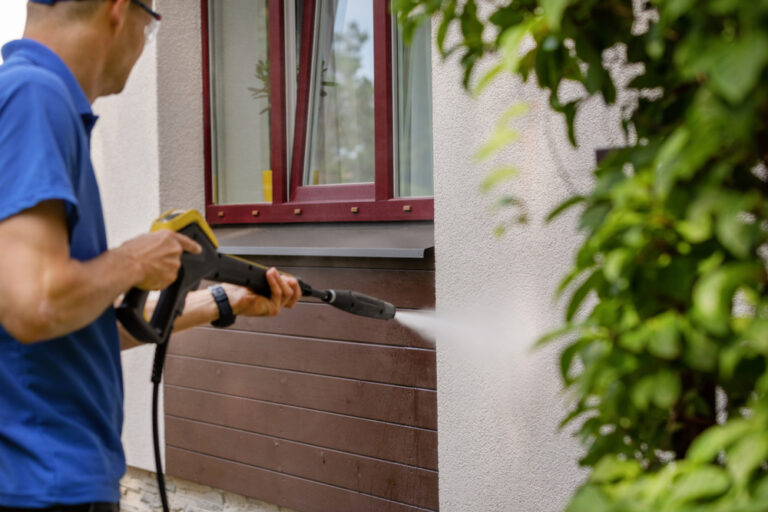 Technician power washing wood siding below a window in Westchester NY for improved curb appeal