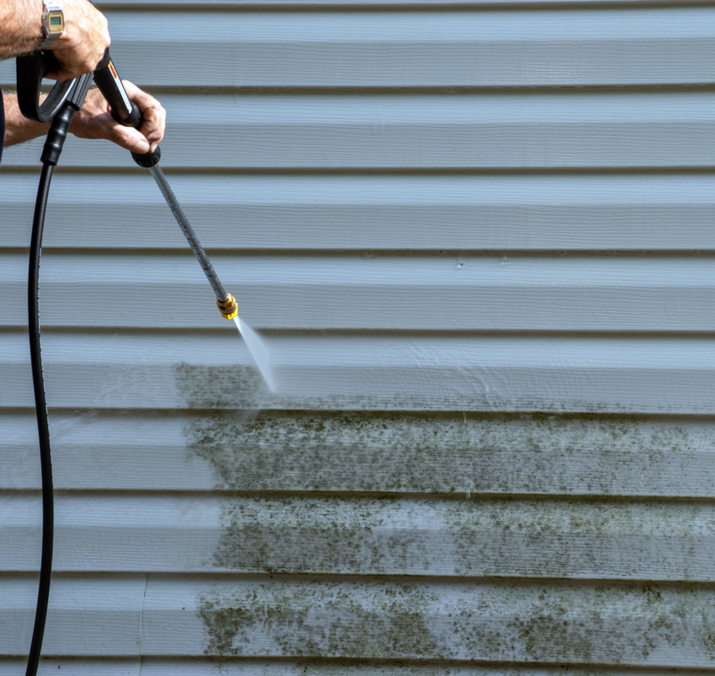 Technician pressure washing green mold from vinyl siding in Westchester NY