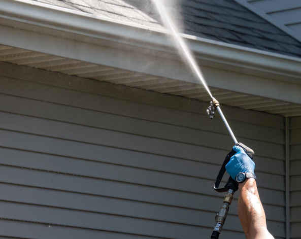 Close-up of a technician using a soft wash nozzle to rinse debris from roof shingles