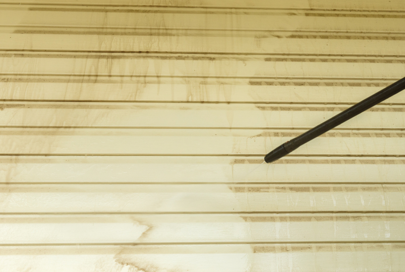 Mid-cleaning vinyl siding with dirt being removed by pressure washer