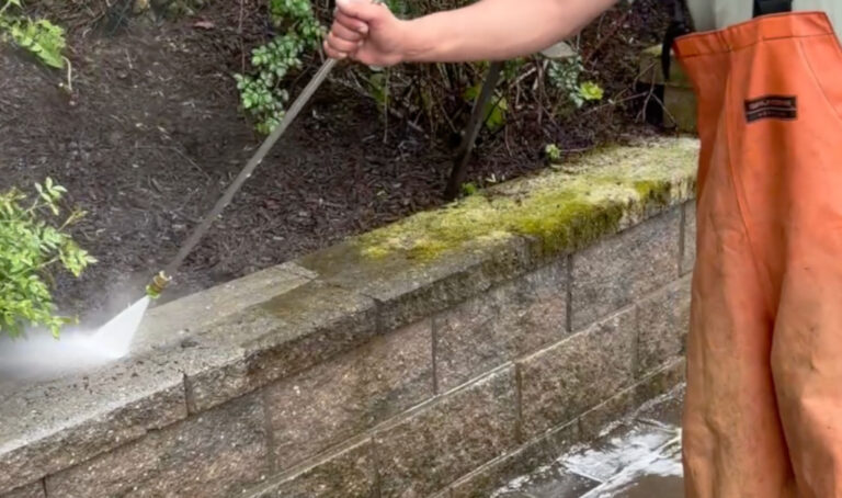 Technician power washing moss-covered retaining wall in Yonkers NY