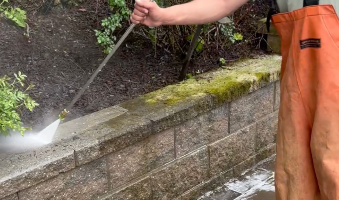 Pressure washing a moss-covered retaining wall in Scarsdale, NY to restore its clean appearance.